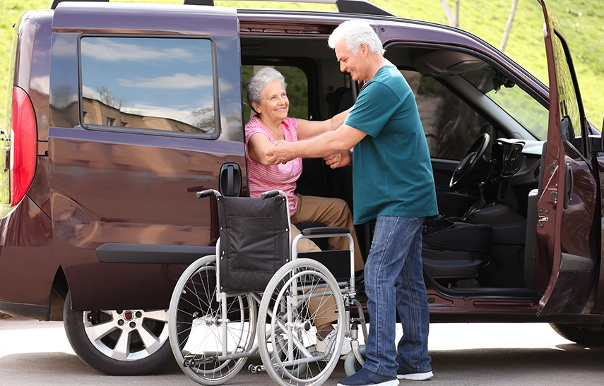 Driver assisting elderly African American woman and Hispanic man into non-emergency medical transport van
